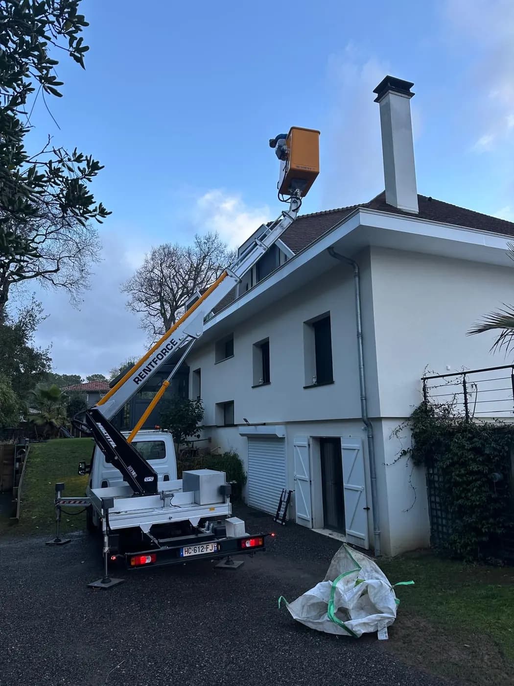 Nacelle élévatrice déployée devant une maison de Biarritz, panier hissé au niveau de la toiture pour le nettoyage de la couverture