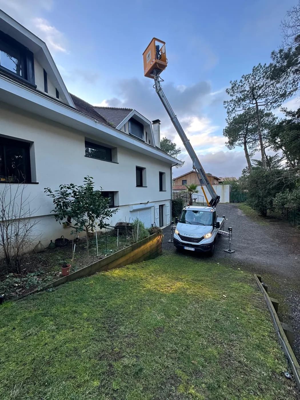 Le chantier vu depuis le jardin : nacelle déployée au-dessus de la toiture, pelouse et massifs préservés au premier plan