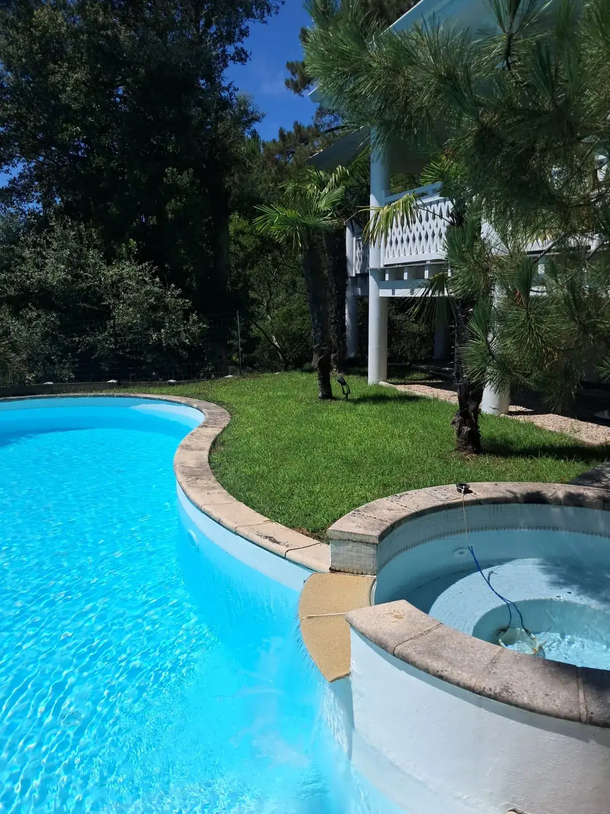 Détail de la piscine et du spa débordant, margelle en pierre reconstituée, pelouse dense en bordure et éclairage de jardin sur piquet